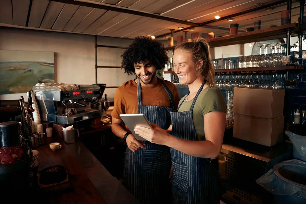 male and female restaurant employees smiling looking at tablet