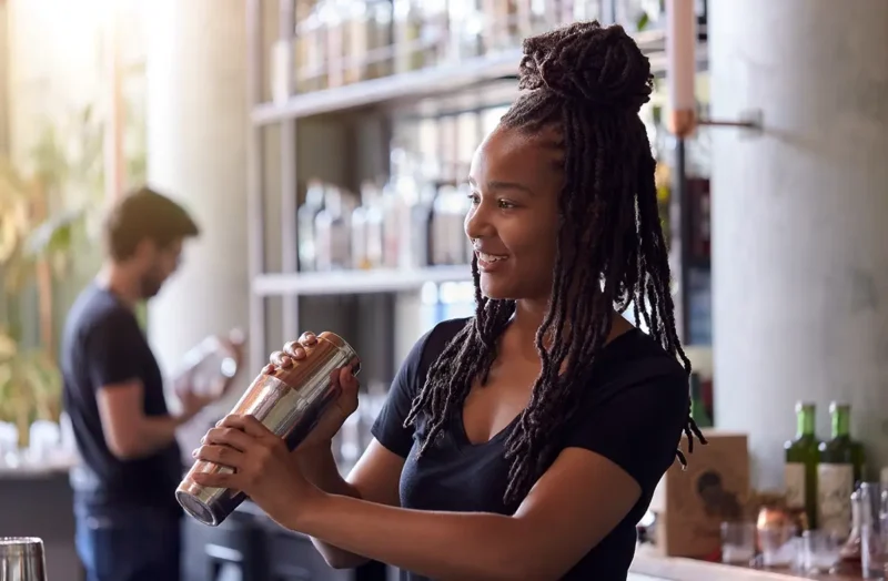 female bartender mixing cocktail in shaker behind bar