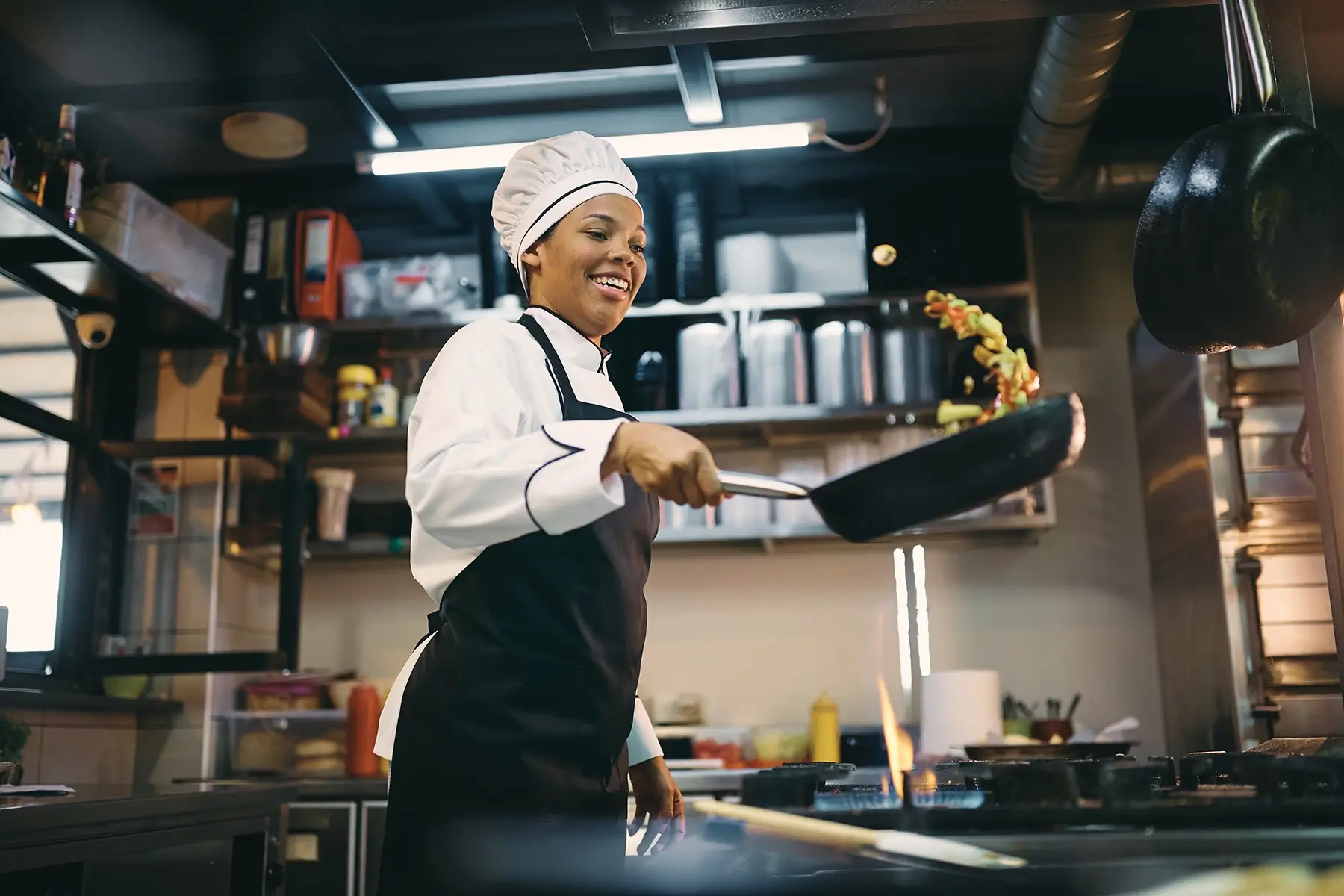 smiling female chef flipping a pan of food