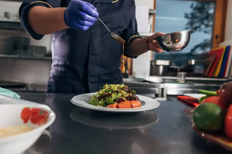 gloved hands of chef drizzling sauce onto entree in kitchen