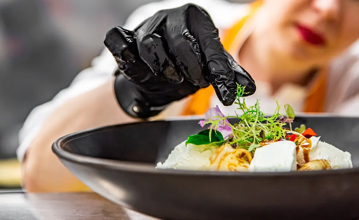 gloved hands of chef adding garnish to dish