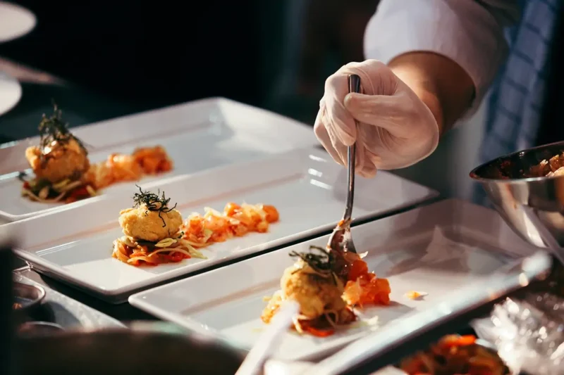 gloved hands of chef adding sauce to several plated dishes