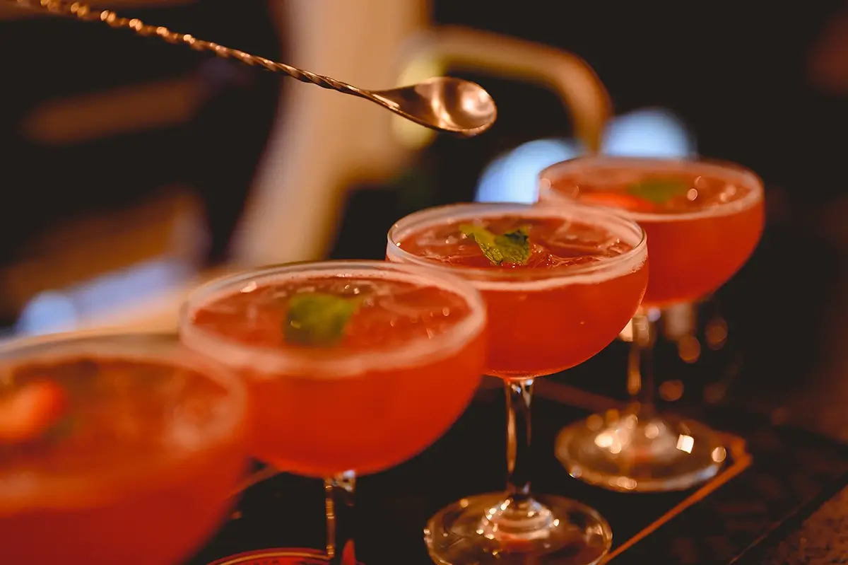 Close-up of glasses filled with red liquid, a stirrer hovering above