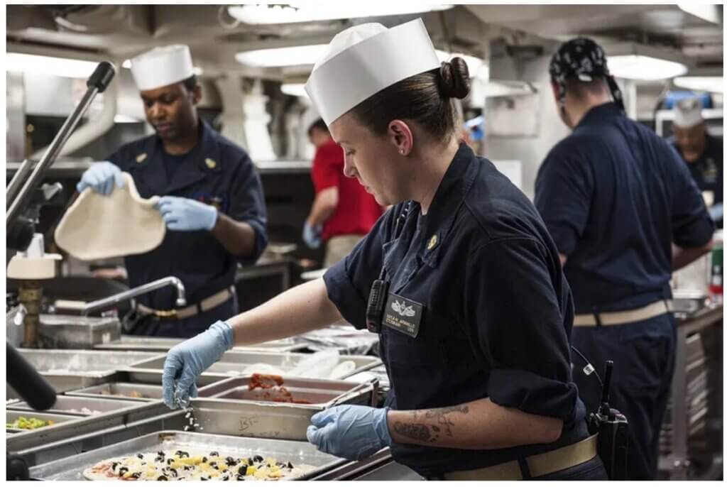 Woman with chef hat sprinkling cheese on a pizza