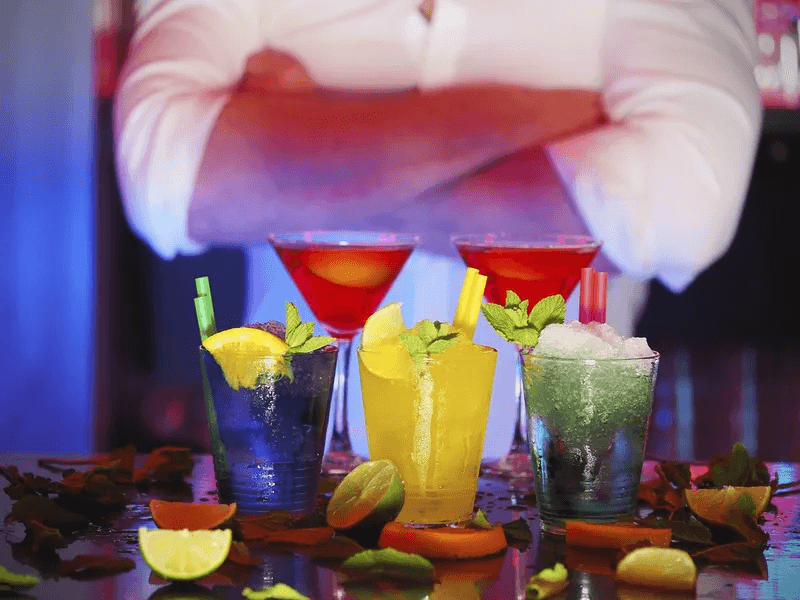 Three colorful beverages with mint and straws, with two red martinis behind them